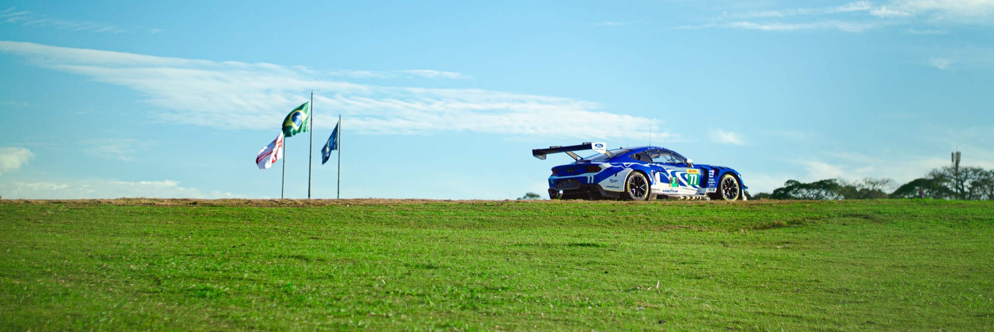 Ford Mustang GT3 #77 recortado na linha do horizonte, ao lado das bandeiras do Brasil e de São Paulo