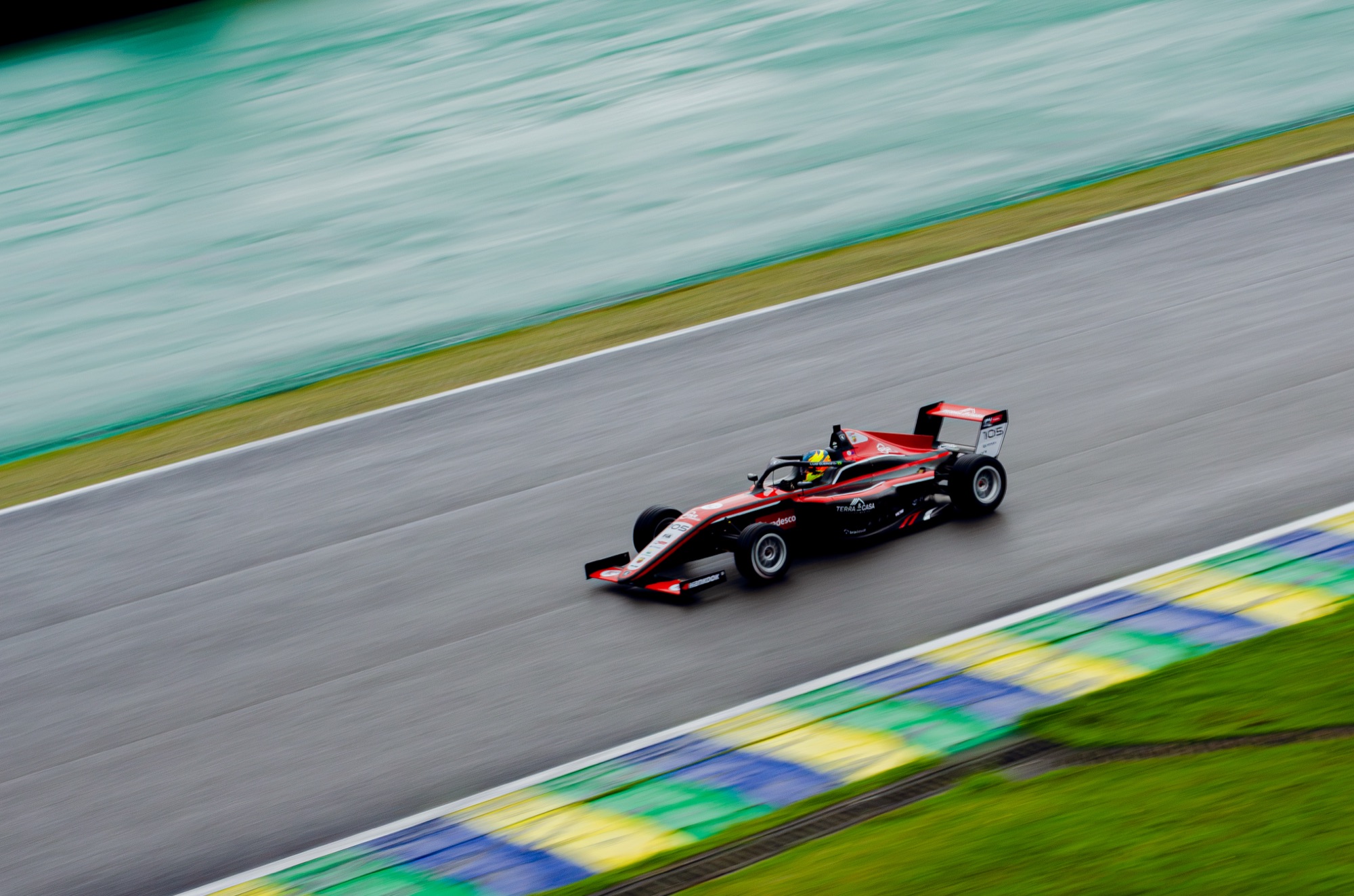 Carro de Fórmula 4 em panning, com as zebras verde, amarela e azul varridas ao fundo